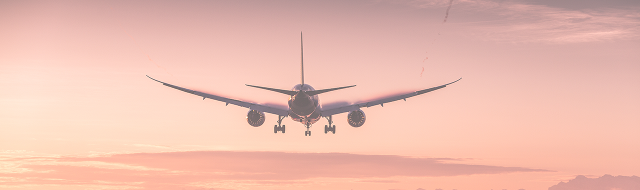 Silhouette of the back of plane taking off and flying away into the orange sunset. 